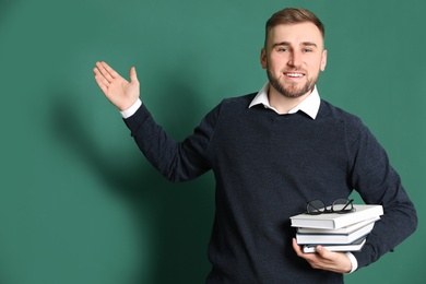 Portrait of young teacher with books on green background
