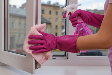 Photo of Young woman cleaning window frame with rag and detergent at home, closeup