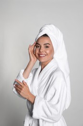 Photo of Beautiful young woman wearing bathrobe and towel on head against light background