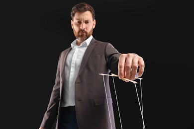Photo of Man in suit pulling strings of puppet on black background, low angle view