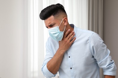 Man in medical mask suffering from pain during breathing indoors