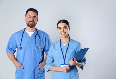 Mature doctor and young nurse against light background