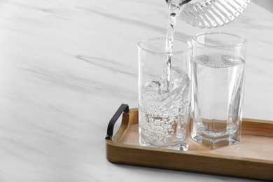 Photo of Pouring water from jug into glass at white marble table. Space for text