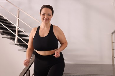 Happy overweight woman in sportswear on stairs indoors, space for text