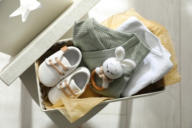 Box with baby clothes, shoes and toy on chair indoors, top view