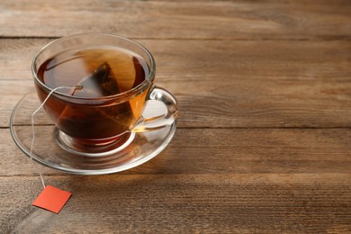 Tea bag in glass cup of hot water on wooden table. Space for text