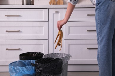 Woman throwing banana peel into trash bin in kitchen, closeup. Separate waste collection