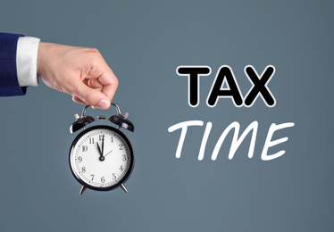 Time to pay taxes. Man holding clock on grey background, closeup