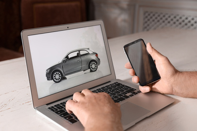 Man using laptop and phone to buy car at wooden table indoors, closeup