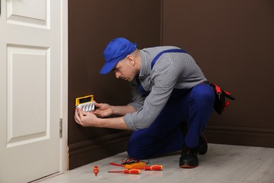 Professional male electrician repairing power socket indoors