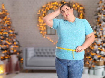 Overweight woman measuring her waist in room with Christmas trees after holidays