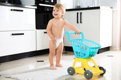 Cute baby with toy walker in kitchen. Learning to walk