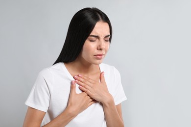 Young woman suffering from breathing problem on light background