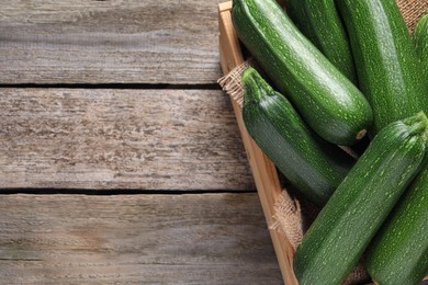Raw ripe zucchinis in crate on wooden table, top view. Space for text