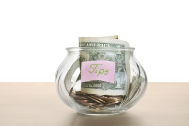 Tip jar with money on wooden table against white background