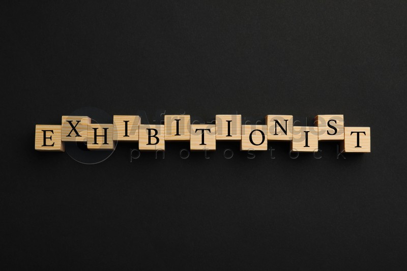 Word EXHIBITIONIST made with wooden cubes on black background, flat lay
