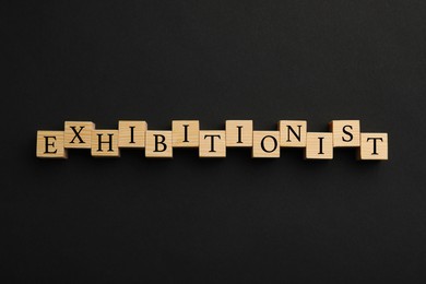 Photo of Word EXHIBITIONIST made with wooden cubes on black background, flat lay