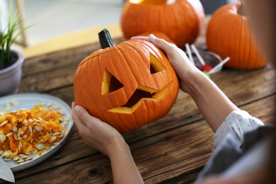 Woman with pumpkin jack o'lantern at wooden table, closeup. Halloween celebration