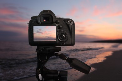 Taking photo of beautiful sandy beach at sunset with camera mounted on tripod