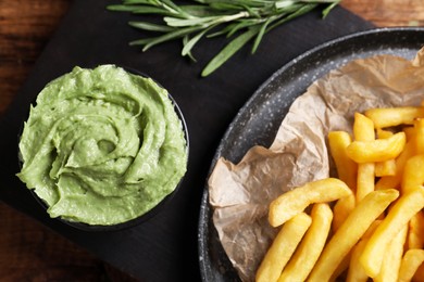 Photo of French fries, avocado dip and rosemary on serving board, top view