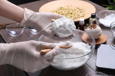 Woman in gloves making bath bomb at wooden table, closeup