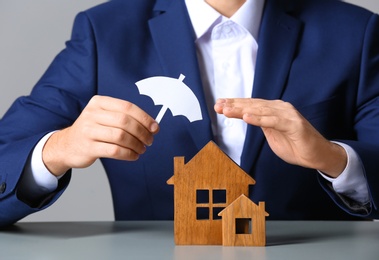 Man covering wooden houses with umbrella cutout at table, closeup. Home insurance