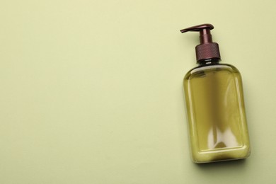 Bottle of shampoo on light green background, top view. Space for text