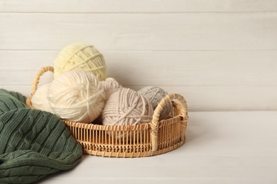 Photo of Woolen yarns in basket on white wooden table. Space for text