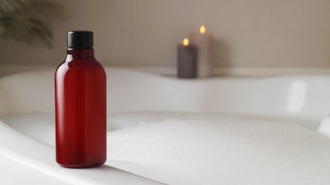 Red bottle of bubble bath on tub indoors, space for text