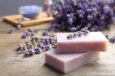 Handmade soap bars with lavender flowers on brown wooden table, closeup. Space for text