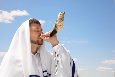 Jewish man in tallit blowing shofar outdoors. Rosh Hashanah celebration