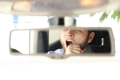 Tired man yawning while driving, reflection in rearview mirror