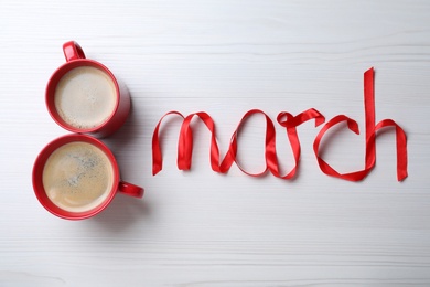 8 March greeting card design with cups of coffee and red ribbon on white wooden background, flat lay. International Women's day