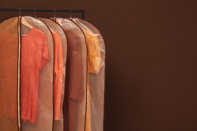 Garment bags with clothes on rack against brown background. Space for text