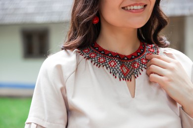 Woman wearing ornate beaded necklace in village, closeup. Ukrainian national jewelry