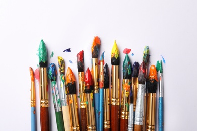 Brushes with colorful paints on white background, flat lay