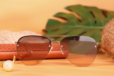 Stylish sunglasses and brown leather case on pale orange background