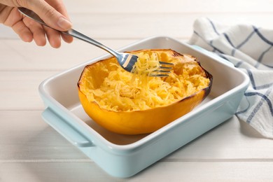 Photo of Woman eating baked spaghetti squash at white wooden table, closeup