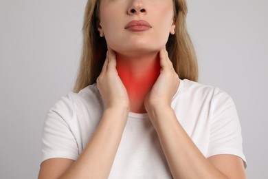 Image of Young woman doing thyroid self examination on light grey background, closeup