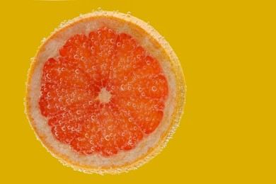 Slice of grapefruit in sparkling water on yellow background. Citrus soda