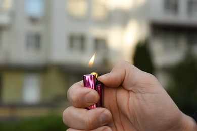 Man holding lighter with burning flame outdoors, closeup