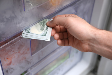 Man hiding money in refrigerator, closeup. Financial savings