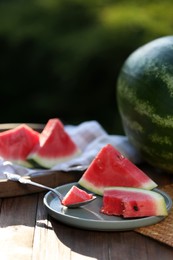Slices of ripe watermelon with spoon on wooden table outdoors