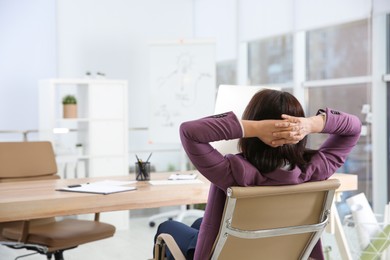 Woman relaxing in office chair at workplace, back view