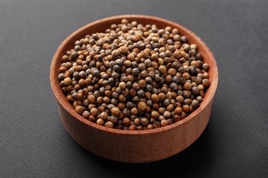 Photo of Wooden bowl of coriander grains on dark background