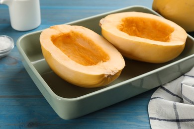 Photo of Raw spaghetti squash halves in baking dish on light blue wooden table, closeup