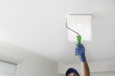 Photo of Handyman painting ceiling with white dye indoors, closeup. Space for text