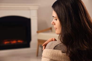 Young woman relaxing near fireplace at home. Space for text