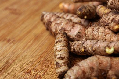 Photo of Many whole turmeric roots on wooden table, closeup. Space for text