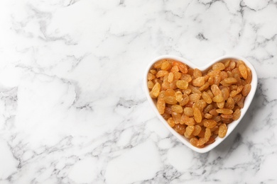 Heart shaped plate with raisins and space for text on marble background, top view. Dried fruit as healthy snack